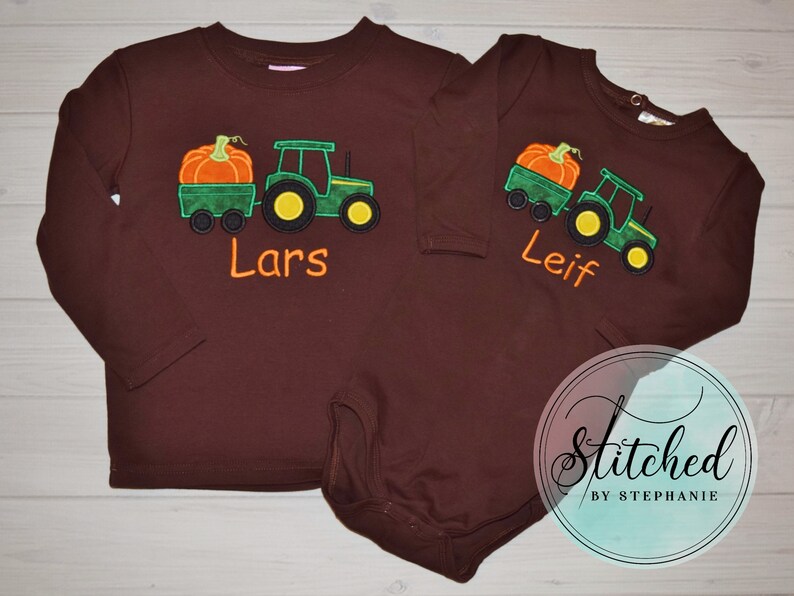 May include: Two brown long-sleeved shirts with a tractor and pumpkin design. One shirt says "Lars" and the other says "Leif" in orange lettering. The tractor is green with yellow wheels, and the pumpkin is orange.