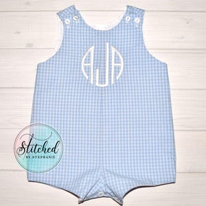 Może przedstawiać: Niebiesko-biały romper w kratę z białym wykończeniem i guzikami. Romper ma biały monogram z literami AJA. Tekst "Stitched by Stephanie" znajduje się w okręgu po lewej stronie u dołu.