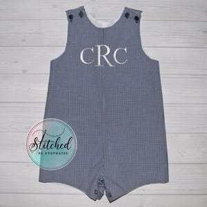 May include: A blue and white gingham romper with the embroidered initials "CRC" in white. The romper has button closures on the shoulders and at the bottom. The logo "Stitched by Stephanie" is in the lower left corner.
