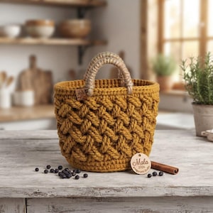 May include: A mustard yellow crocheted basket with a thick, textured braided pattern and a sturdy jute-wrapped handle. A small wooden tag attached to the side reads "Mala," and a round wooden disc at the base is inscribed with "Mala 2026 amigurumi studio."