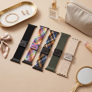 May include: Five braided watch bands with metal buckles arranged in a row. The bands are black, multicolored, dark patterned, olive green, and beige. Each band features a distinct woven texture and a metallic clasp mechanism for secure attachment.