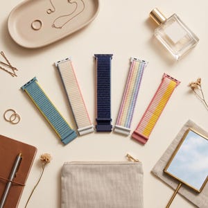 May include: Five woven watch bands arranged in a fan shape. The bands feature various colors including blue with yellow, cream with pink, solid navy blue, a multi-colored pastel rainbow stripe, and a pink band with a yellow section.