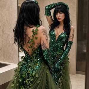 Peut inclure: Une robe longue vert émeraude à sequins avec un décolleté en V profond, des gants assortis à sequins longs jusqu'aux coudes et une surjupe en tulle vert olive ornée de vignes de lierre artificielles descendant dans le dos et sur le corsage.