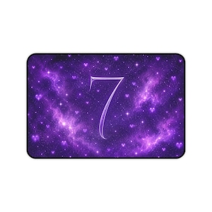 May include: A rectangular desk mat featuring a deep purple galaxy background with swirling nebula clouds, scattered white stars, and small purple heart shapes. The center of the mat displays a large, stylized white number seven with a thin outline.