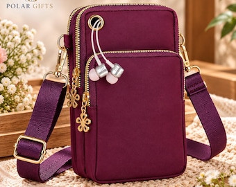 Könnte beinhalten: Eine dunkelviolette Umhängetasche mit mehreren Reißverschlussfächern, goldfarbenen Beschlägen und einem passenden verstellbaren Riemen. Die Tasche verfügt über eine kleine runde Öffnung für kabelgebundene Ohrhörer und blumenförmige Reißverschlussanhänger.