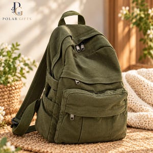 Könnte beinhalten: Ein olivgrüner Rucksack aus Segeltuch mit einem Tragegriff, verstellbaren Schultergurten, einem Hauptfach mit Reißverschluss und einer kleineren Reißverschlusstasche auf der Vorderseite. Der Rucksack hat Seitentaschen und silberfarbene Metallreißverschlüsse.