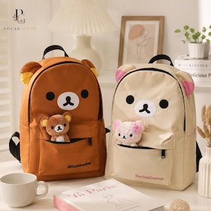 Puede incluir: Dos mochilas con diseños de osos. La mochila de la izquierda es marrón con orejas amarillas y un pequeño oso de peluche en el bolsillo delantero. La mochila de la derecha es crema con orejas rosas y un pequeño oso de peluche.