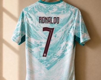 May include: A short-sleeved sports jersey featuring a white and light blue abstract wave pattern. The back displays the name RONALDO in dark red lettering above the large dark red number 7, which includes a small emblem at the bottom.