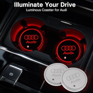 May include: Two circular, silver-toned luminous coasters featuring the Audi logo and text. The coasters are shown both inactive and illuminated with a bright red glow inside a vehicle cup holder, with the text Illuminate Your Drive above.