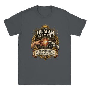 May include: A charcoal gray t-shirt featuring a graphic print of a human hand and a robotic hand reaching toward each other. The text reads THE HUMAN ELEMENT and AI CAN GENERATE. YOU DECIDE WHAT MATTERS. The design includes gold laurel leaves.