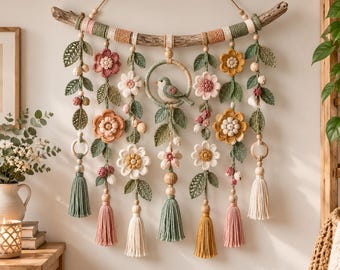 May include: A wall hanging featuring a driftwood branch adorned with crocheted flowers, green leaves, and small berries. A central circular hoop contains a crocheted bird. The piece includes hanging strands with wooden beads and colorful tassels.