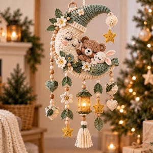 May include: A crochet wall hanging featuring a crescent moon with a sleeping face, a brown bear, and a white rabbit. The moon is decorated with green leaves and white flowers. Dangling elements include wooden beads, crochet stars, hearts, and a lantern.