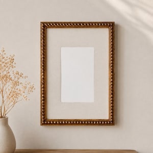 May include: A rectangular picture frame with a metallic bronze finish and a beaded texture along the inner and outer edges. The frame contains a light beige mat board surrounding a centred, blank, rectangular white space for a photograph.