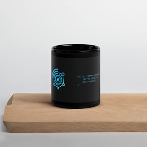May include: A black ceramic mug featuring a bright blue graphic of a connected network node icon and the printed code snippet: while (coffee.isEmpty) { coffee.refill(); brain.synk(); } in a light blue font on the side of the mug.