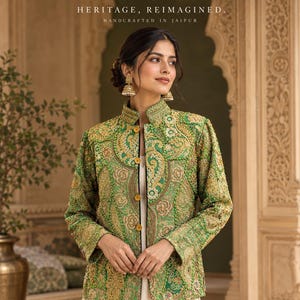 May include: A green jacket featuring intricate gold embroidery and a high collar with yellow buttons. The text BIG BOUNDS, HERITAGE, REIMAGINED, and HANDCRAFTED IN JAIPUR is displayed at the top of the image above the jacket.