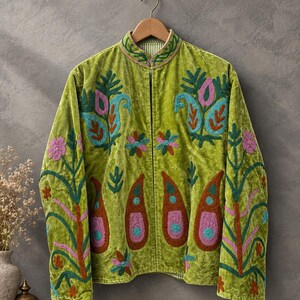 Könnte beinhalten: Eine lindgrüne Samtjacke mit Stehkragen und langen Ärmeln. Das Kleidungsstück ist mit aufwendigen, mehrfarbigen Blumen- und Paisley-Stickereien in den Farbtönen Pink, Türkis, Orange und Dunkelgrün auf der Vorderseite und den Ärmeln verziert.