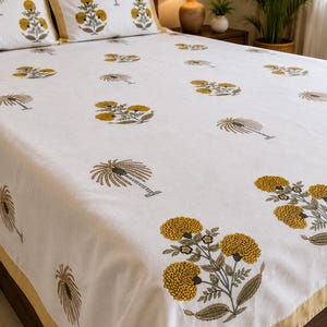 May include: A white bed sheet and two matching pillowcases featuring a repeating pattern of yellow marigold flower clusters and grey palm trees. The bedding set includes a solid mustard yellow border trim along the edges of the pillows and sheet.