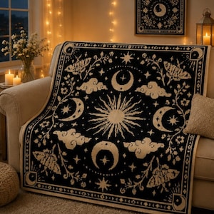 May include: A black and cream woven throw blanket featuring a central sun motif surrounded by crescent moons, stars, clouds, and moth illustrations. The rectangular textile has a decorative border pattern and a repeating celestial design throughout.