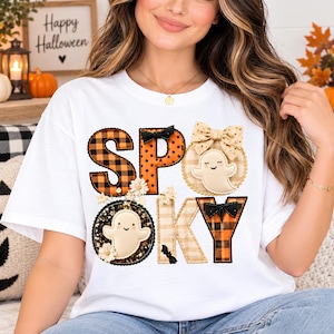 May include: A white t-shirt featuring the word SPOOKY in large letters. The letters are decorated with orange and black buffalo plaid, polka dots, and beige gingham patterns. Two small cream-colored ghosts, black bows, and small white flowers are attached.