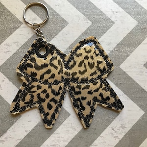 May include: A black and gold leopard print bow keychain with a silver key ring.