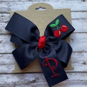 May include: A navy blue hair bow with a red cherry embroidery and the letter "P" in red thread.