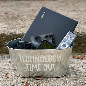May include: A silver metal container with the words "Technology Time Out" printed on the side. The container is filled with various electronic devices, including a laptop, a cell phone, and a remote control.