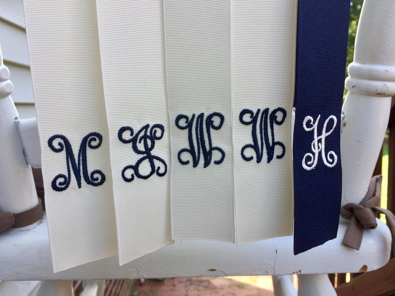 May include: Five white satin ribbons with navy blue embroidered initials, M, S, W, W, and H.
