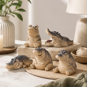 May include: A collection of five small, textured alligator figurines in varying poses. Two are sitting upright, one is lying flat with its mouth open, one is lying flat with its mouth closed, and one is sitting with a rounded, stout body shape.