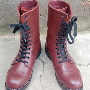 Peut inclure: Une paire de bottes mi-mollet d'un bordeaux profond avec une finition lisse, des lacets noirs et un bout rapporté orné de perforations décoratives subtiles le long de la couture. Les bottes ont une semelle noire robuste et des surpiqûres blanches.