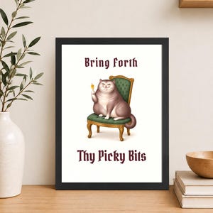 May include: A framed wall art print featuring a plump, light brown cat sitting on a green upholstered chair with gold legs. The cat holds a small yellow snack. The text "Bring Forth" appears above the cat, and "Thy Picky Bits" is printed below.