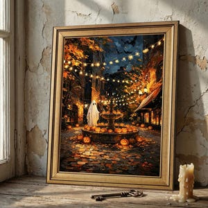May include: A framed wall art print depicting a night scene with a white ghost standing by a stone fountain surrounded by numerous glowing orange jack-o'-lanterns, autumn leaves on the ground, and string lights hanging above in a dark street.