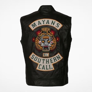 May include: A black leather vest featuring a large embroidered patch on the back. The patch displays a central Mayan-inspired mask graphic with red, gold, and grey tones, flanked by arched banners reading MAYANS and SOUTHERN CALI. M.C. is centered.