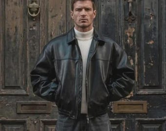 May include: A black leather jacket with a front zipper closure and a pointed collar, worn over a white ribbed turtleneck sweater and dark grey denim jeans. The garment features long sleeves with cuffs and a straight hemline at the waist.