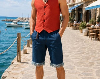 Könnte beinhalten: Ein Strohhut mit rotem Band und Kinnriemen, eine ärmellose rostfarbene Weste mit drei schwarzen Knöpfen und eine dunkelblaue Jeansshorts mit ausgefranstem Saum, kombiniert mit einfachen schwarzen Zehentrennern für einen sommerlichen Look.