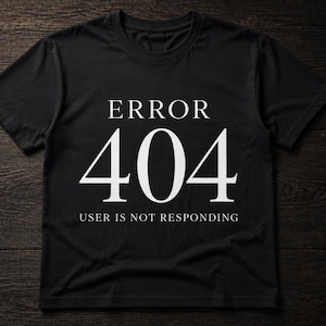Könnte beinhalten: Ein schwarzes T-Shirt mit kurzen Ärmeln und dem weißen Text ERROR 404 USER IS NOT RESPONDING. Das Shirt hat einen Rundhalsausschnitt und besteht aus einfarbigem schwarzem Stoff, wobei die Grafik in einer weißen Serifenschrift mittig auf der Brust gedruckt ist.