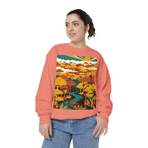 May include: A coral-coloured crewneck sweatshirt featuring a rectangular graphic print of a jungle landscape. The illustration depicts a winding river, a small boat with passengers, dense trees, and a sun in a retro colour palette of orange, yellow, and teal.