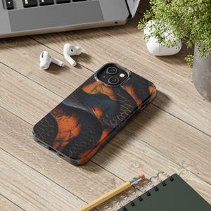 May include: A smartphone case featuring a dark, abstract pattern of black and orange interlocking shapes with a subtle hexagonal grid texture. The case has a dual-camera cutout on the back and covers the rear and sides of the mobile device.