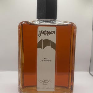 Puede incluir: Un frasco de vidrio rectangular de agua de tocador Yatagan de Caron Paris. El frasco contiene un líquido de color ámbar y presenta una etiqueta vertical blanca con texto negro y una tapa negra. La etiqueta indica un volumen de 500 ml.