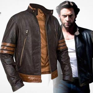 May include: A dark brown leather jacket featuring a stand-up collar, a front zip fastening, and two horizontal tan stripes on each sleeve. The jacket includes two zipped chest pockets and a tan leather hem, with a tan interior lining visible.