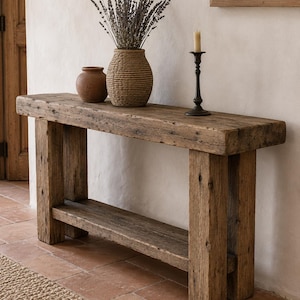 May include: A rectangular console table crafted from weathered brown wood with a thick top, four sturdy legs, and a lower shelf. On the table sits a small brown ceramic pot, a textured woven vase filled with dried lavender, and a dark metal candle holder.