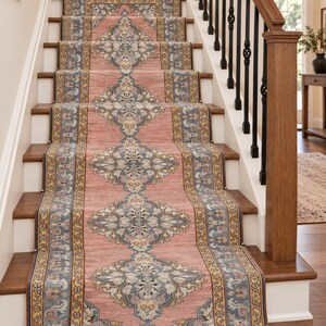 May include: A long stair runner rug featuring a dusty pink center with repeating blue and cream floral medallion patterns. The border is detailed with intricate blue and yellow geometric motifs, covering the wooden steps of a staircase.