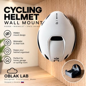 May include: A white cycling helmet wall mount with black accents, featuring the text CYCLING HELMET WALL MOUNT, OBLAK LAB, and RCR. The mount is shown attached to a wood-grain surface, with a small inset image displaying the black mounting bracket.