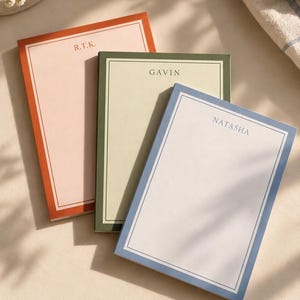 May include: Three rectangular notepads with colored borders and personalized text. The first is light pink with an orange border and the initials R.T.K. The second is light green with a dark green border and the name GAVIN. The third is white with a blue border and the name NATASHA.
