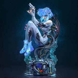 Può includere: Una statuetta dettagliata di un personaggio con capelli blu iridescenti, che indossa una tuta bianca con componenti meccanici e cavi. La figura impugna una piccola pistola, siede su una complessa base industriale e brilla di luce blu.