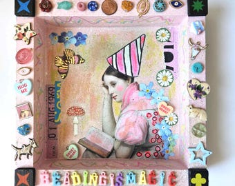 Könnte beinhalten: Ein rosa Tablett mit weißem Hintergrund und einem Mädchen, das ein Buch liest. Das Tablett ist mit bunten Perlen, Knöpfen und anderen Kleinigkeiten verziert. Das Mädchen trägt ein rosa Kleid und einen gestreiften Hut. Der Text "Reading is Magic" ist in bunten Buchstaben am unteren Rand des Tabletts geschrieben.