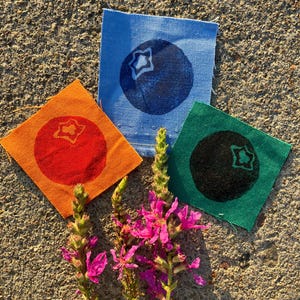 May include: Three square fabric patches featuring screen-printed berry illustrations. One patch is light blue with a dark blue berry, one is orange with a red berry, and one is green with a black berry. Each berry has a star-shaped top detail.