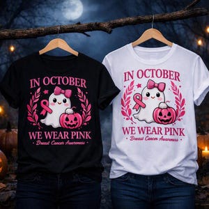 Op de afbeelding: Een zwart t-shirt en een wit t-shirt, elk met een afbeelding van een witte geest met een roze strik, een roze lint en een roze pompoen. De tekst luidt IN OCTOBER WE WEAR PINK en Breast Cancer Awareness in roze letters.