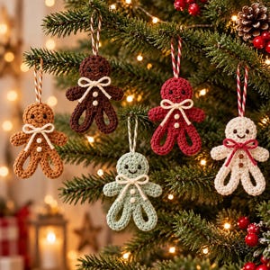May include: Five crocheted gingerbread person ornaments hanging from a Christmas tree. The ornaments are light brown, dark brown, red, mint green, and white. Each figure features a small bow at the neck, two white or red buttons, and a hanging string.