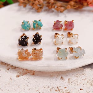 Peut inclure: Une collection de huit boucles d'oreilles à clous avec des pierres précieuses brutes et non polies dans diverses couleurs, dont turquoise, rose, noir, blanc, ambre et vert pâle. Chaque pierre est fixée dans une monture en métal doré.