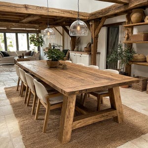 May include: A large rectangular dining table made of reclaimed wood with a thick top and sturdy trestle base. The table is surrounded by six chairs with light-coloured upholstered seats and wooden frames, positioned under two glass pendant lights.
